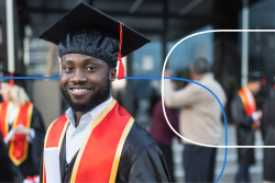 Smiling graduate in cap and gown at an outdoor graduation ceremony with peers in the background