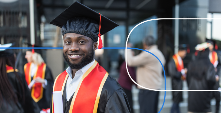 Smiling graduate in cap and gown at an outdoor graduation ceremony with peers in the background